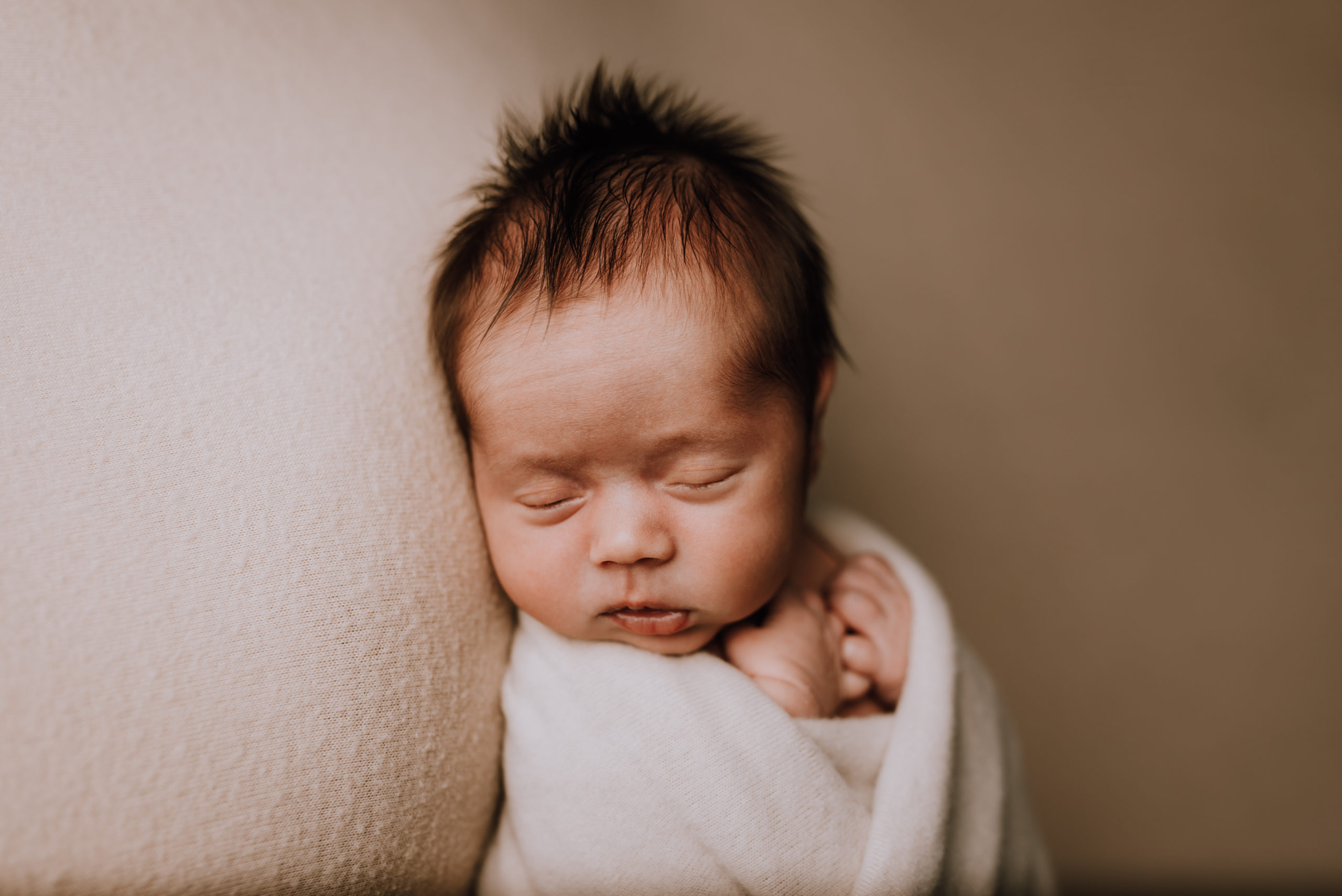 newborn baby wrapped in cream color with hair