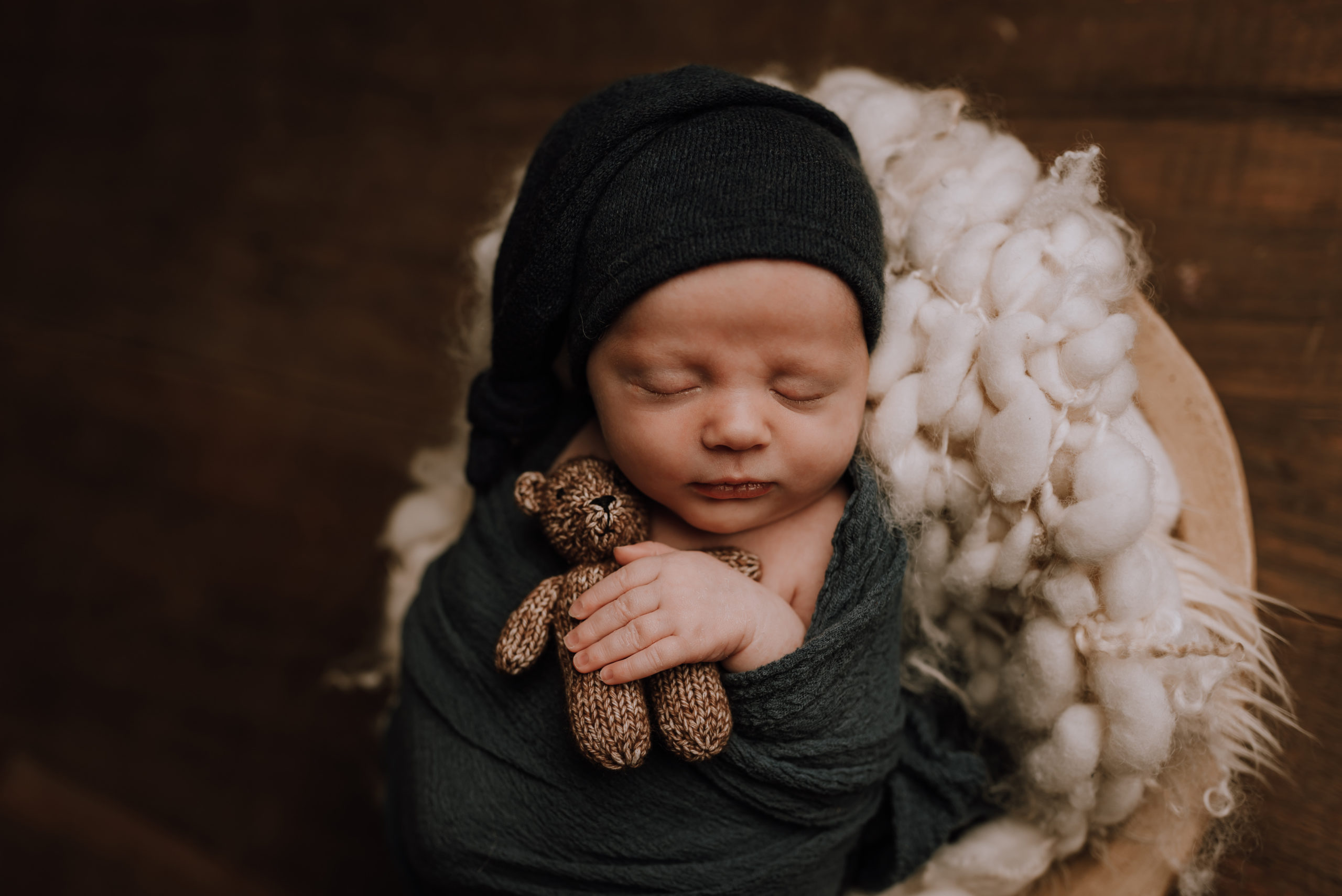newborn baby wrapped in green and wearing a cap holding a teddy bear Kitchener Baby Stores